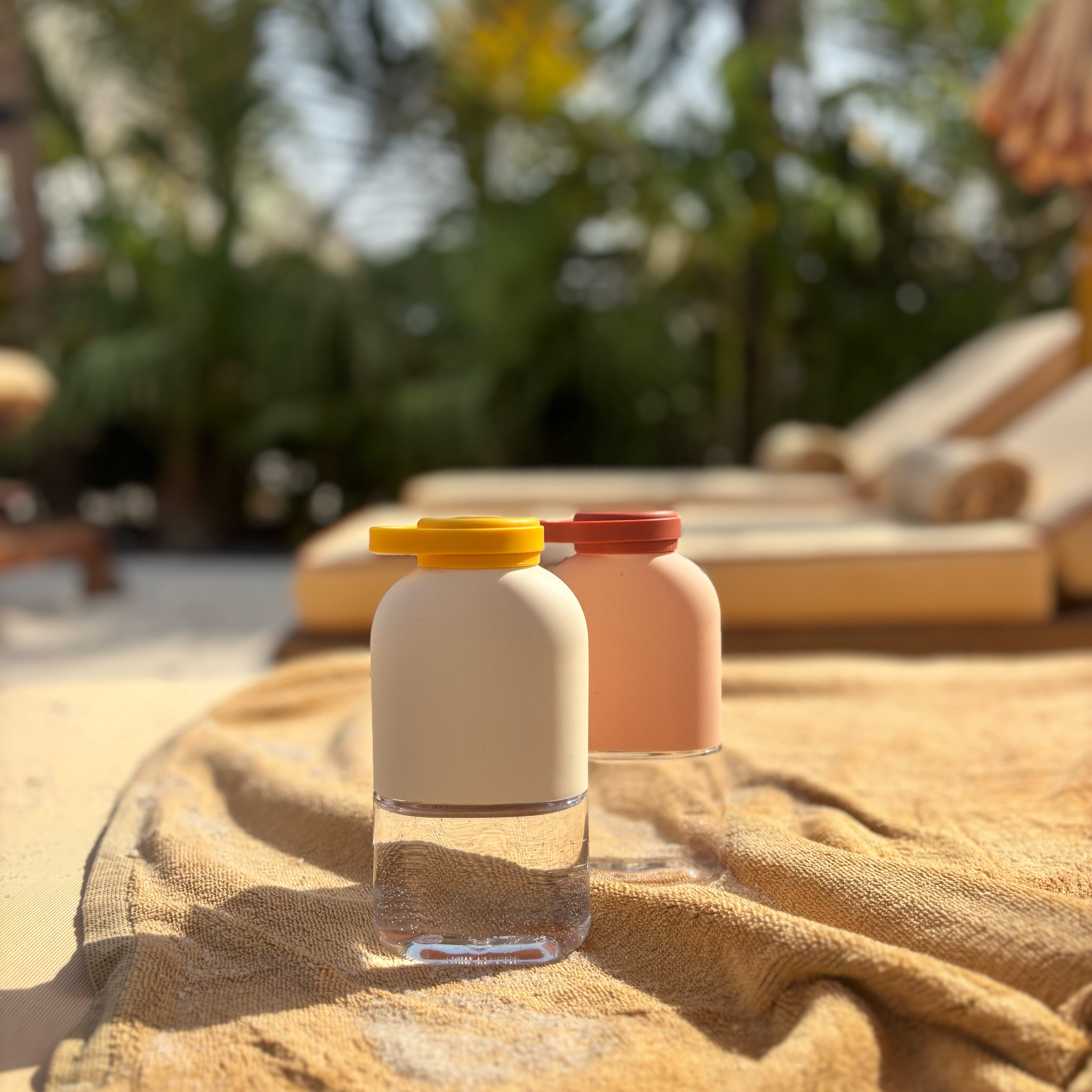 Two bottles with yellow and red lids on a textured surface with blurred greenery in the background